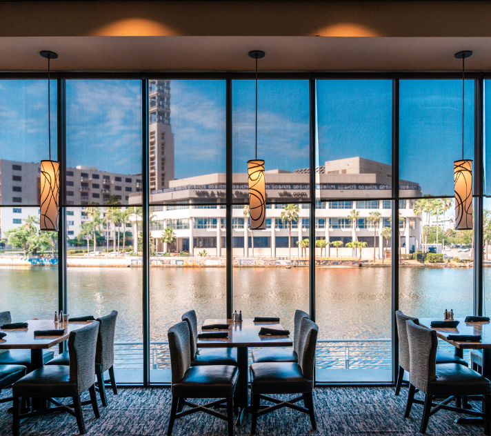 a room with tables and chairs and a large window with a view of a city and water