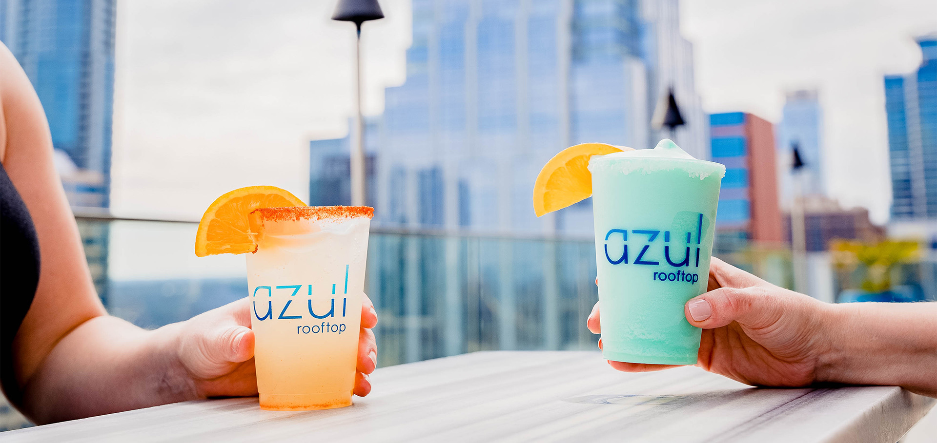 Close up of blue frozen cocktail, and orange colored cocktail with orange slices on rim