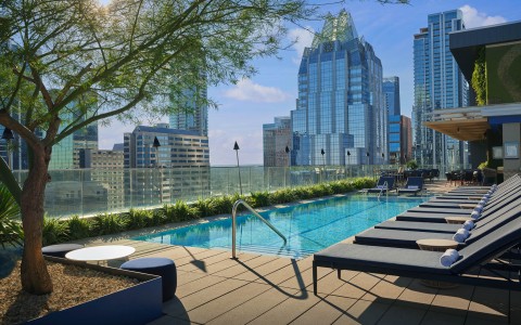 a pool with chairs and a tree in front of a city