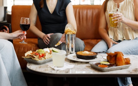 a group of people sitting on a couch with food and drinks