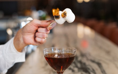 a hand holding a skewer over a drink