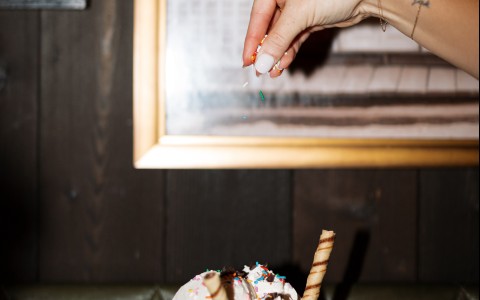 a hand sprinkling a piece of ice cream in a glass bowl