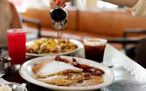 a person pouring syrup on a plate of pancakes