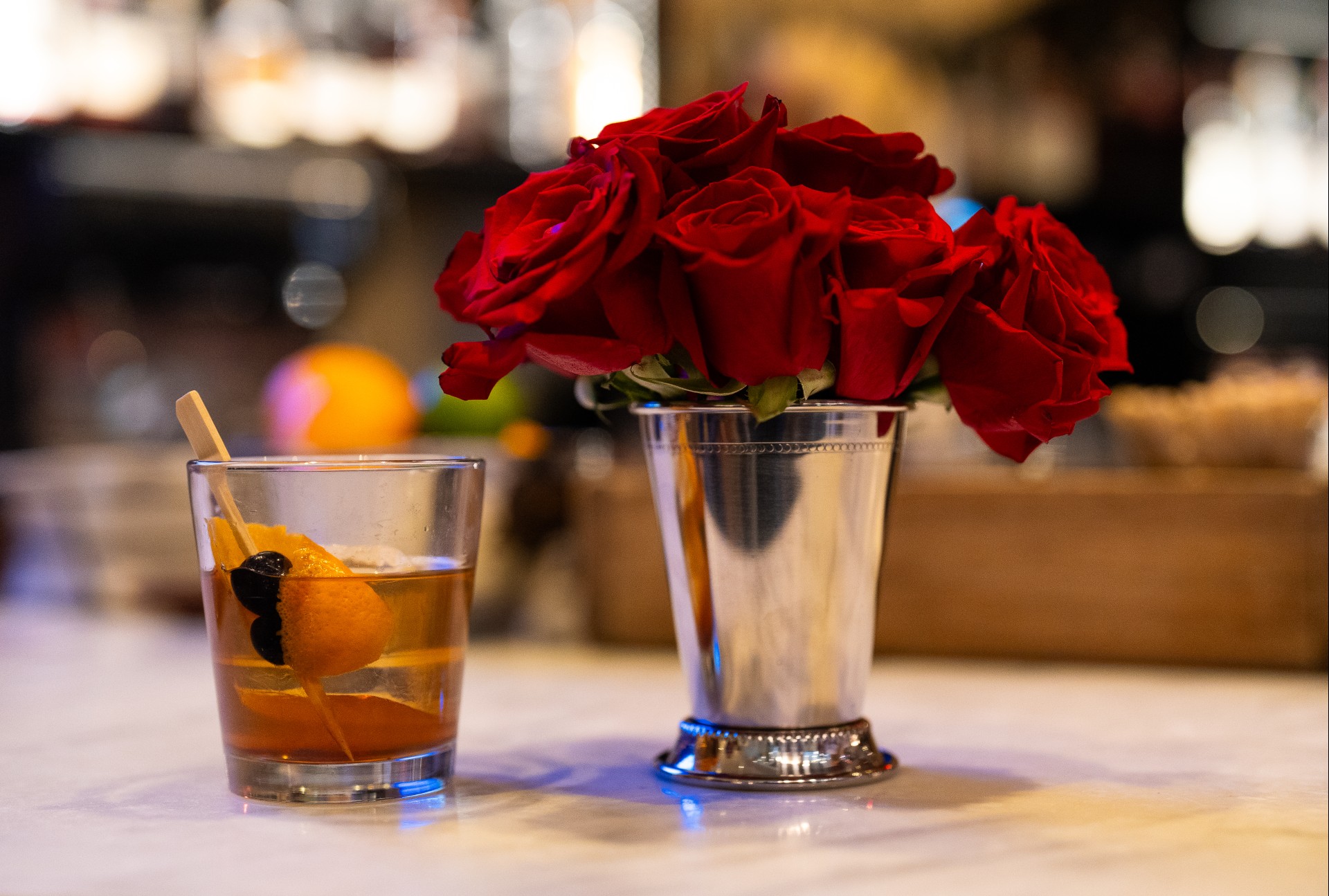 a bouquet of roses in a silver cup next to a glass of liquid