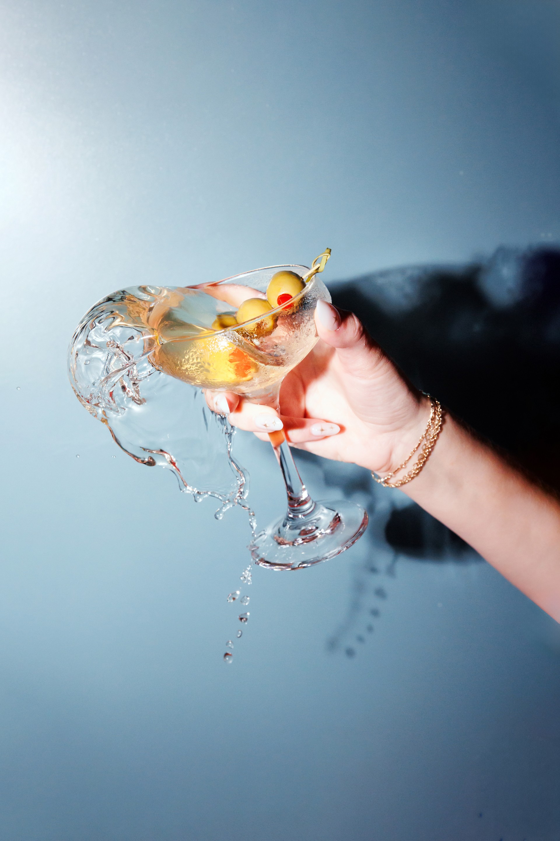 a hand holding a glass with liquid and olives