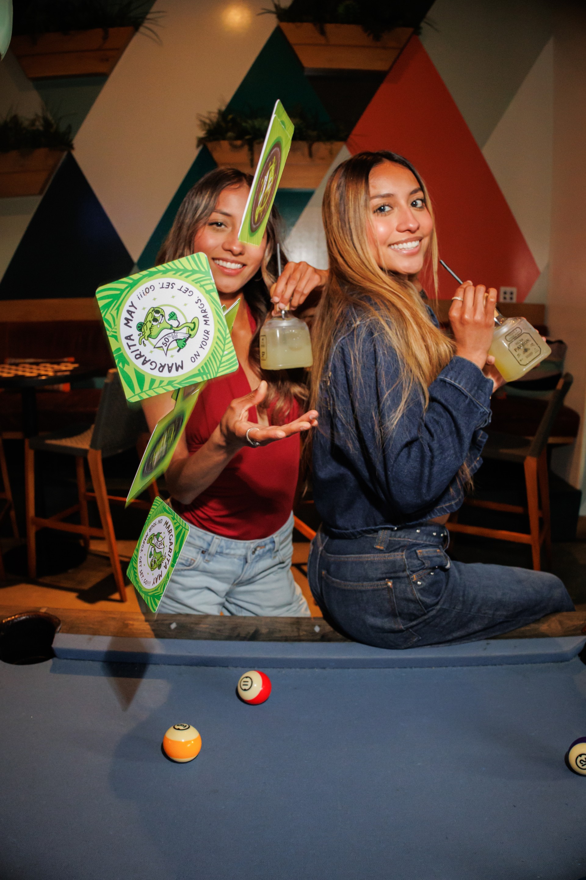 two women sitting back to back holding drinks