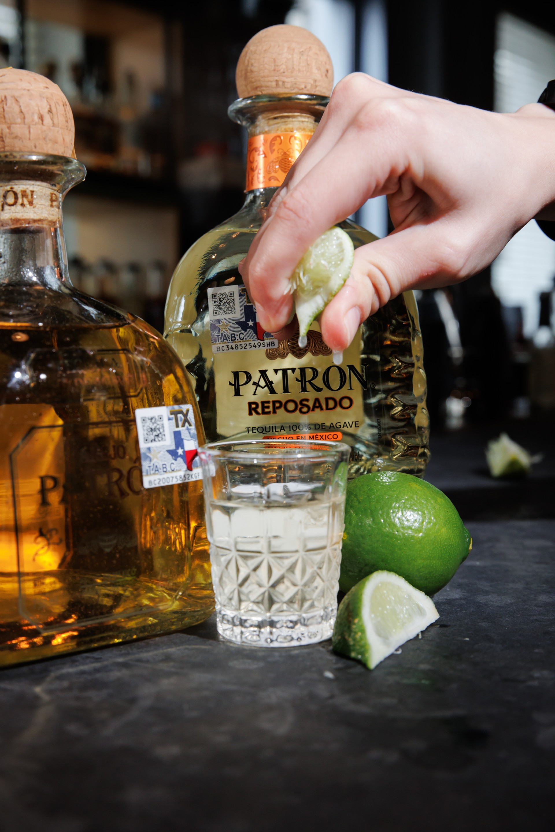 a hand squeezing a lime into a shot glass