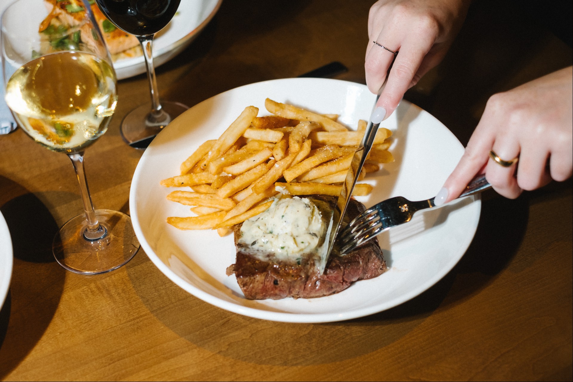 a person cutting a steak with a knife and fork on a plate with french fries