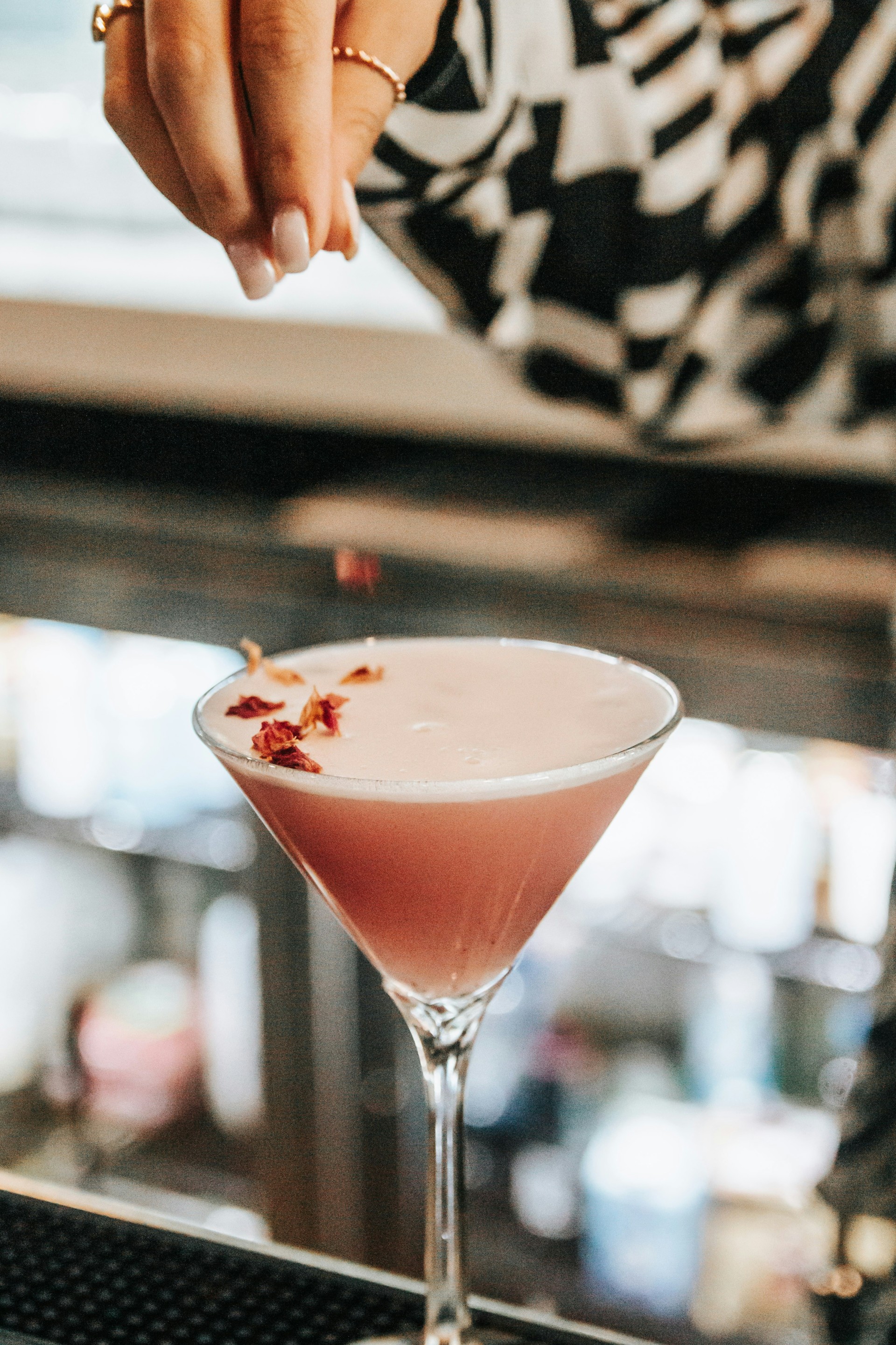a hand pouring a pink drink into a martini glass