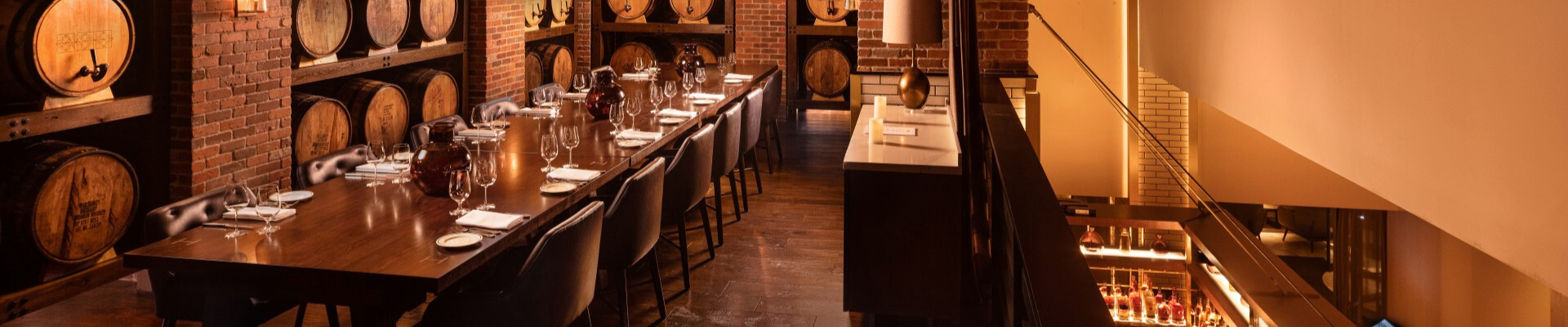 a long table with wine glasses and chairs in a room with brick walls