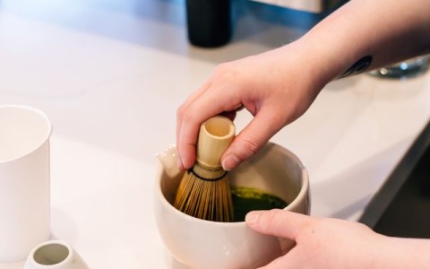 a person using a whisk to mix green tea