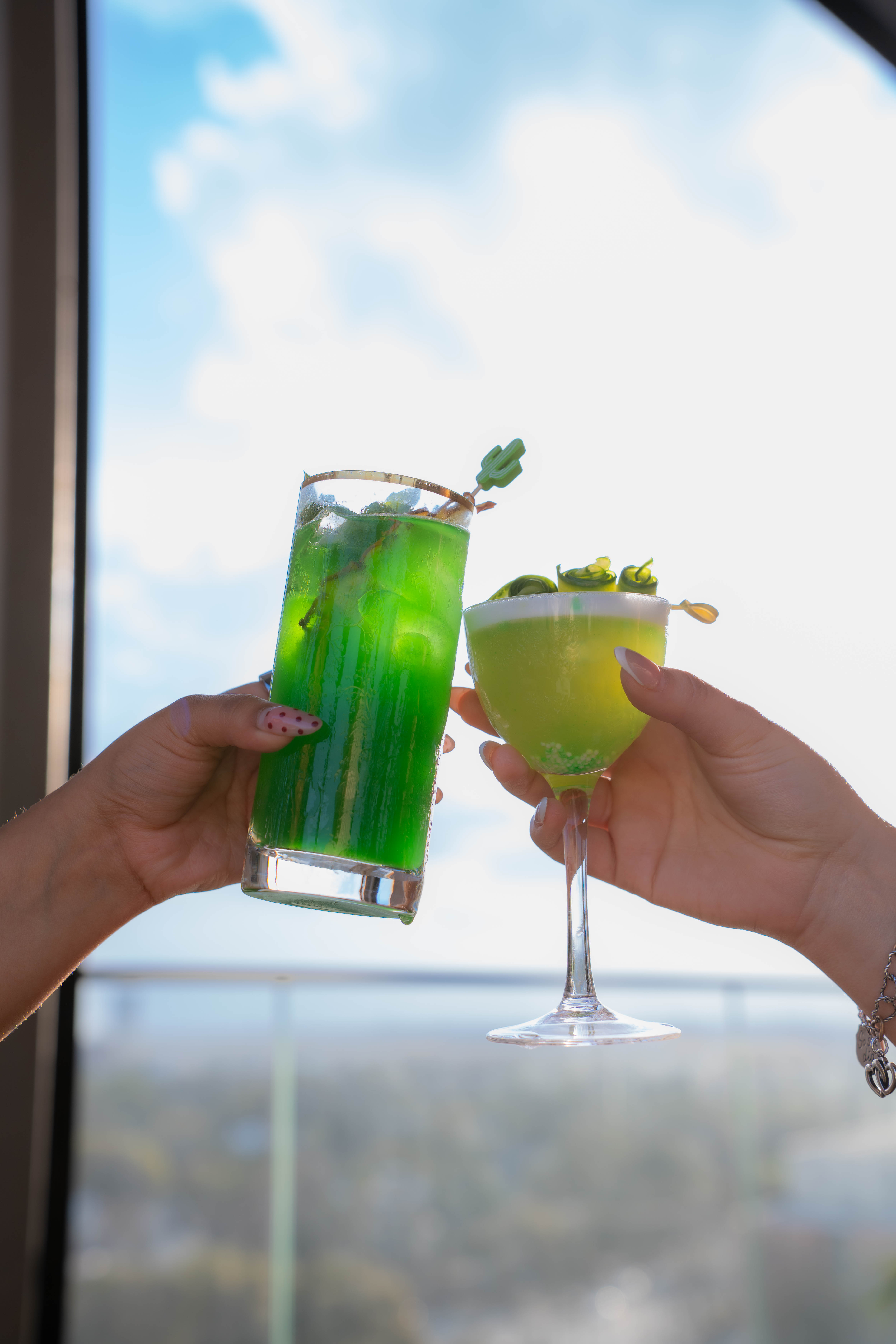 a pair of hands holding up a pair of glasses with green liquid