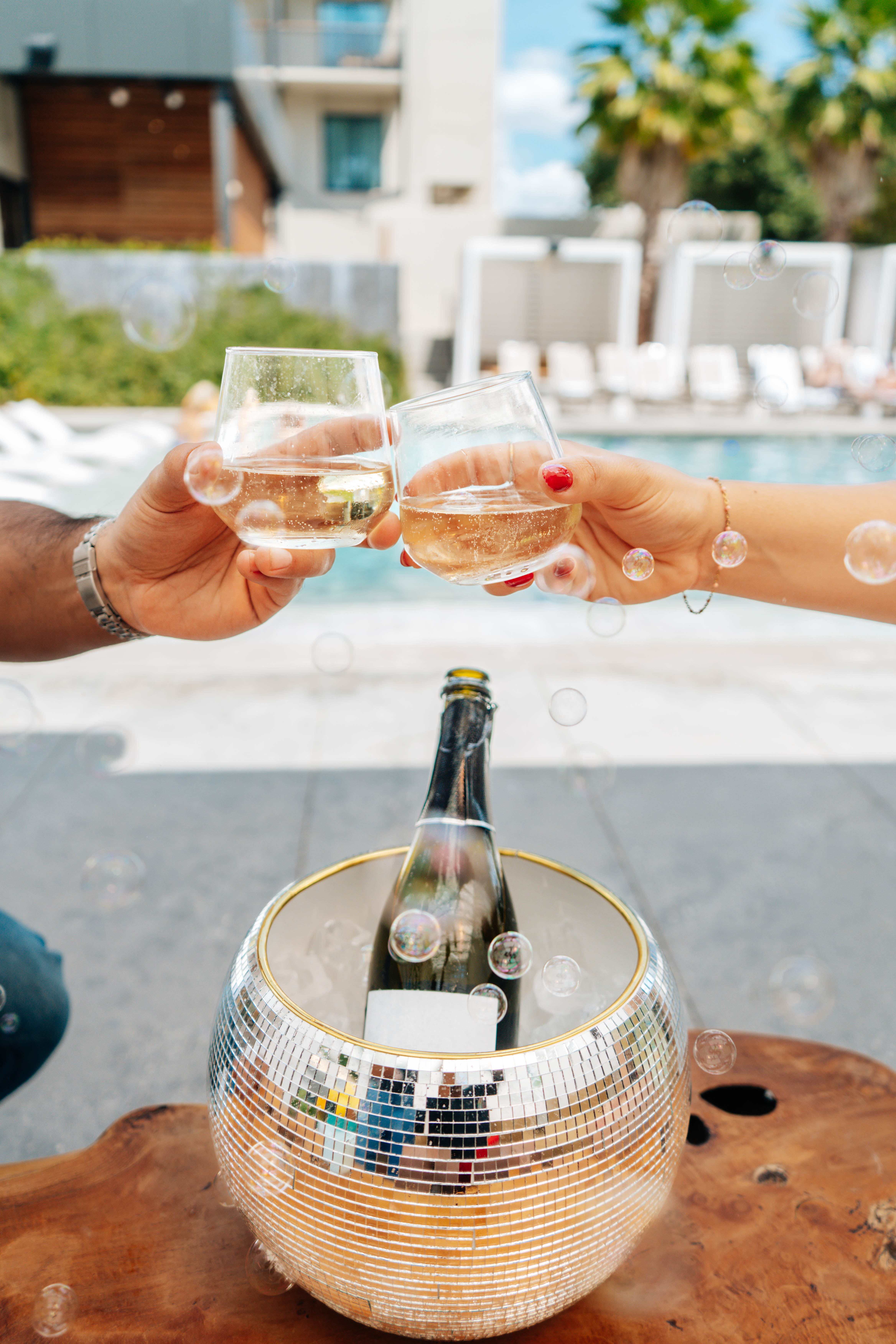 a couple of hands holding glasses with liquid in front of a bottle