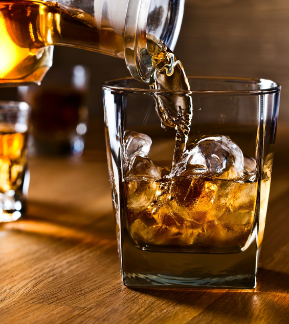 a glass with ice and amber liquid being poured into it