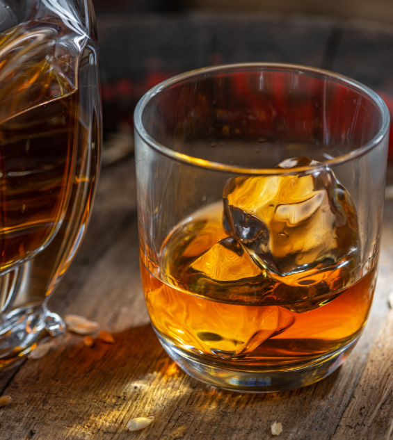 a glass of amber liquid with ice and a pitcher of whiskey