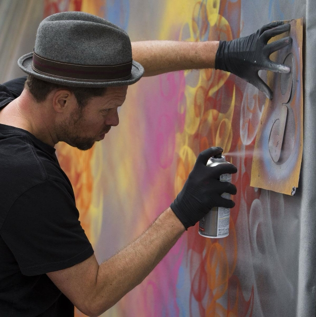 a man wearing a hat and black gloves painting a wall