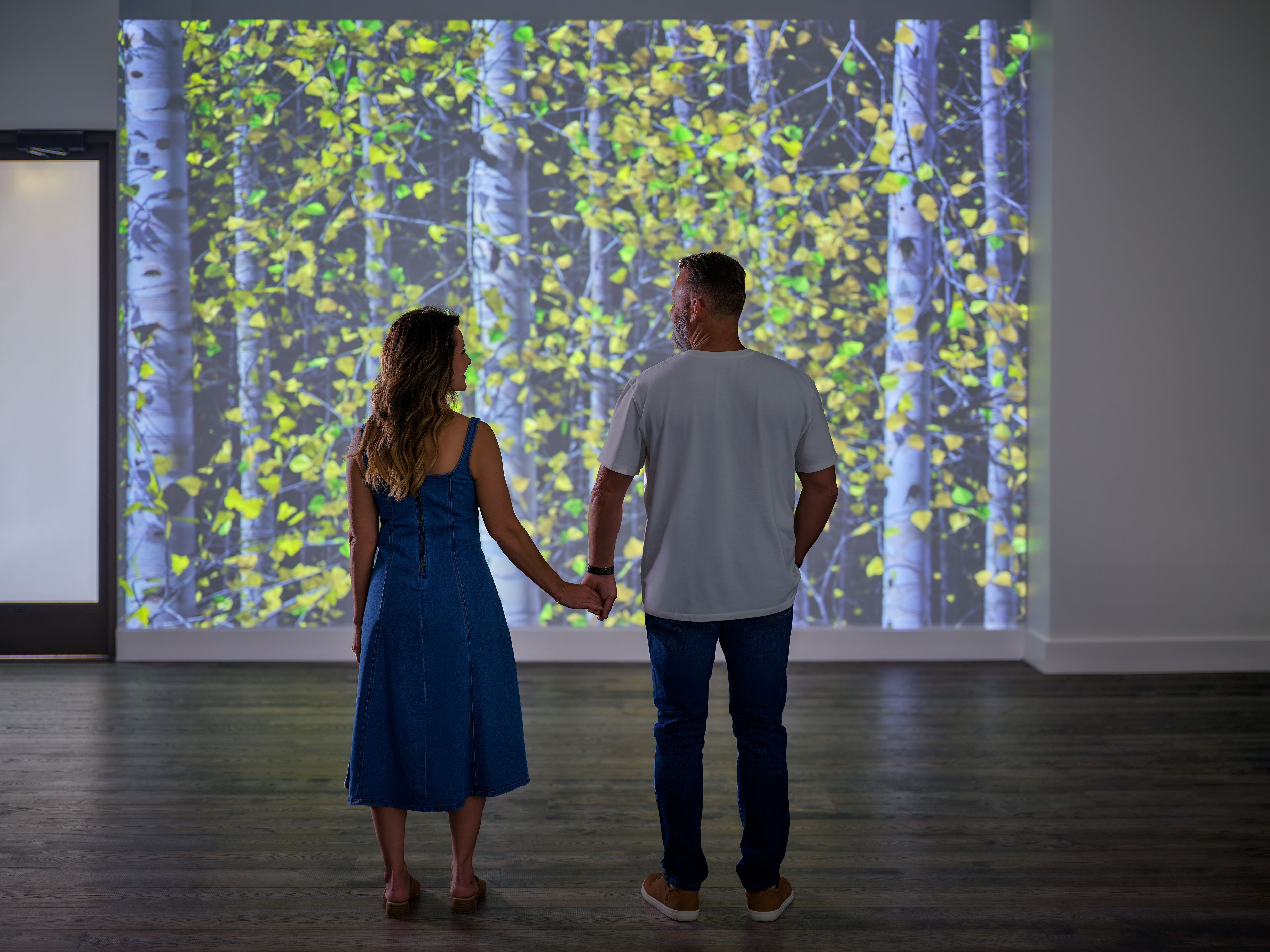 a man and woman holding hands looking at a large screen