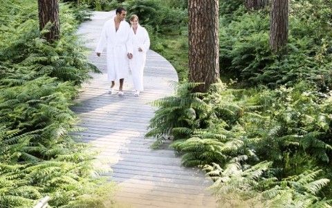 a man and woman in white robes walking on a path in a forest