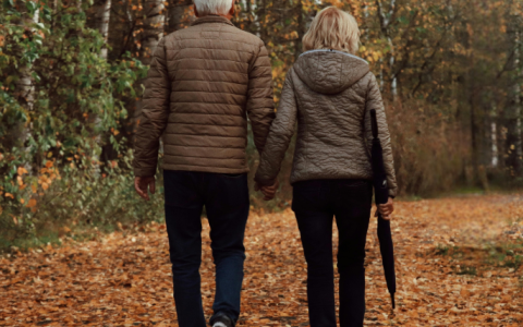 a man and woman holding hands walking on a path with trees