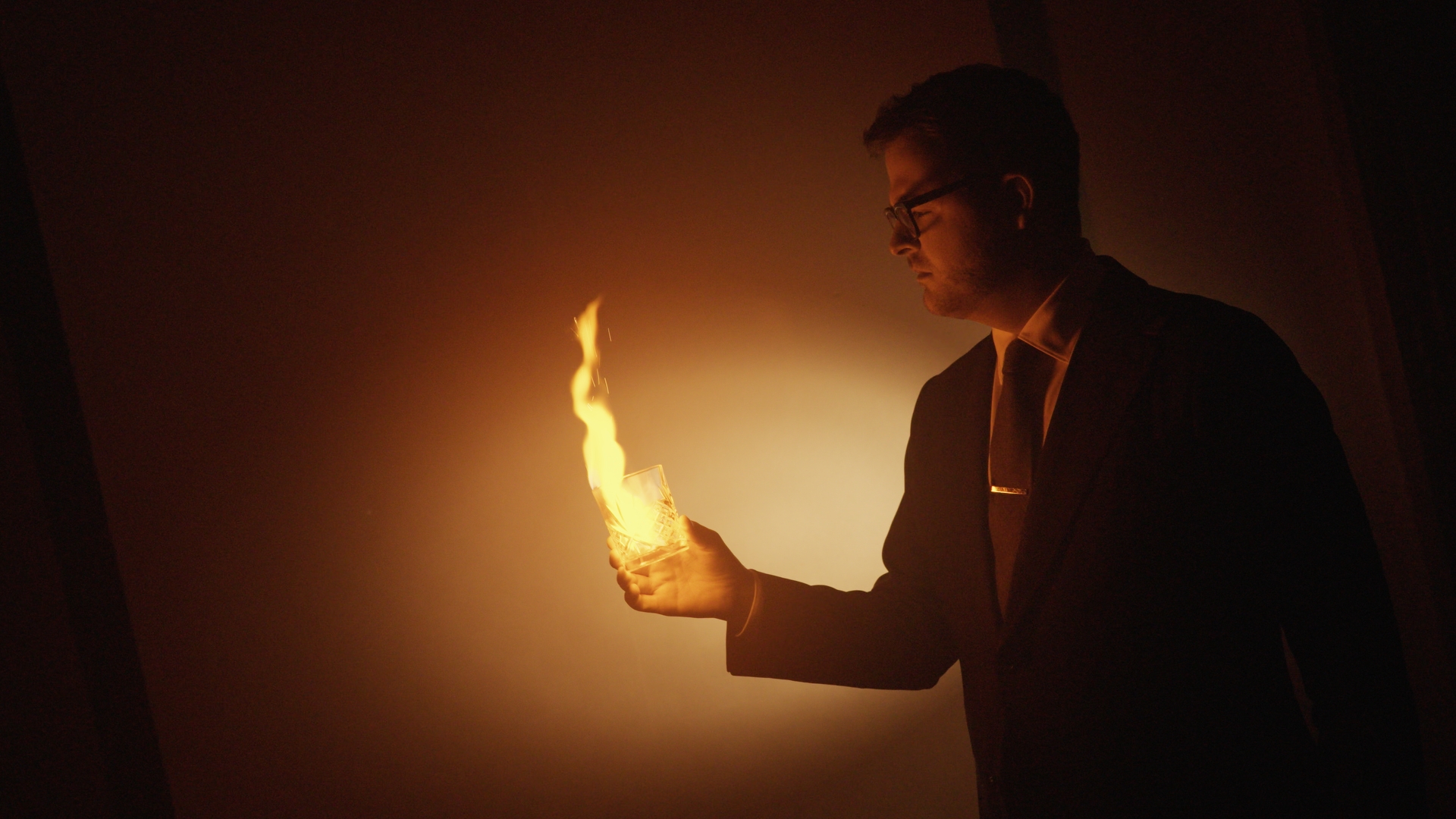 a man holding a glass with a fire in his hand