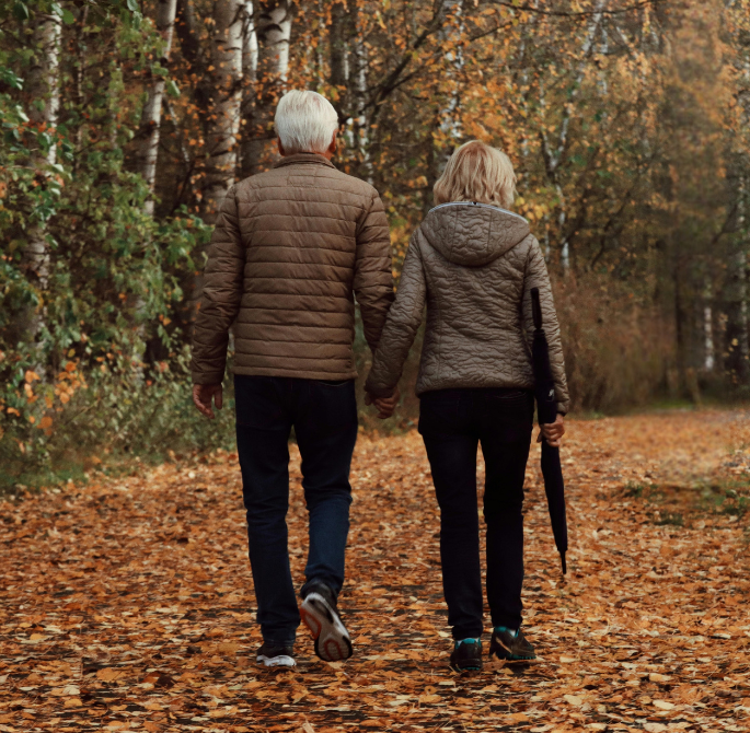 a man and woman holding hands walking on a path with trees