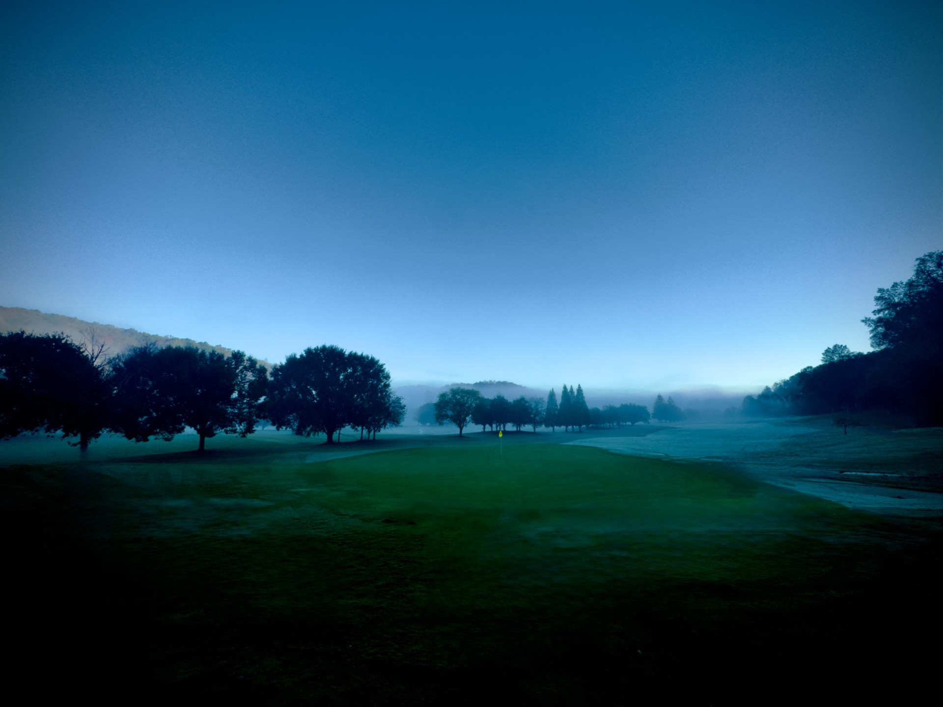 a foggy landscape with trees and a field