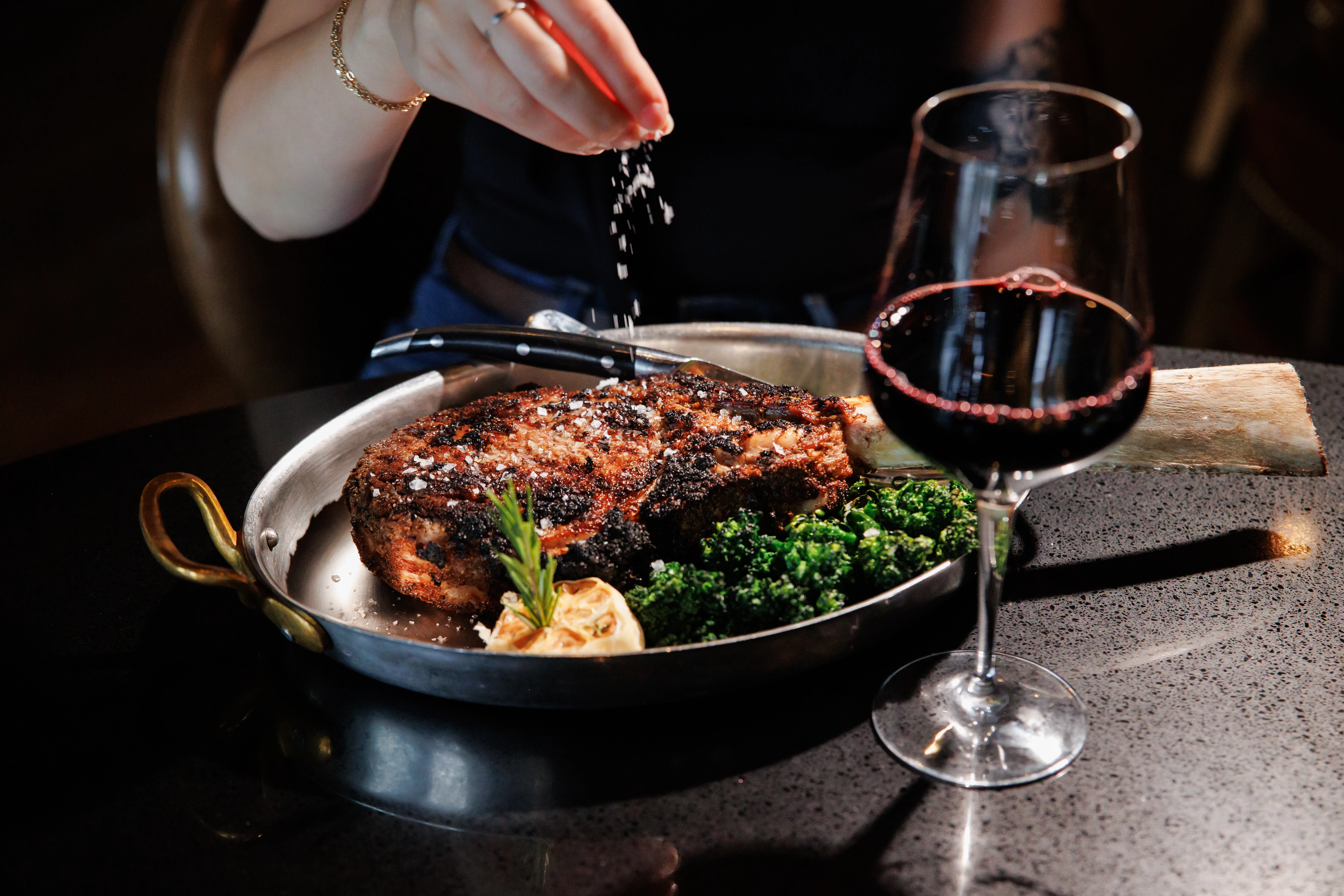 a person sprinkling salt on a plate of meat and vegetables