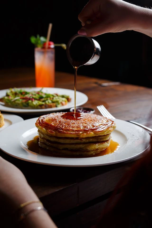 a person pouring syrup on a stack of pancakes