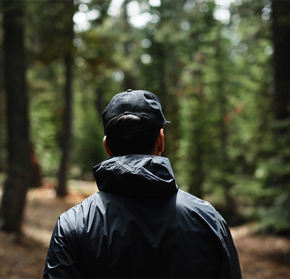 Man with jacket and hat walking through thick forest