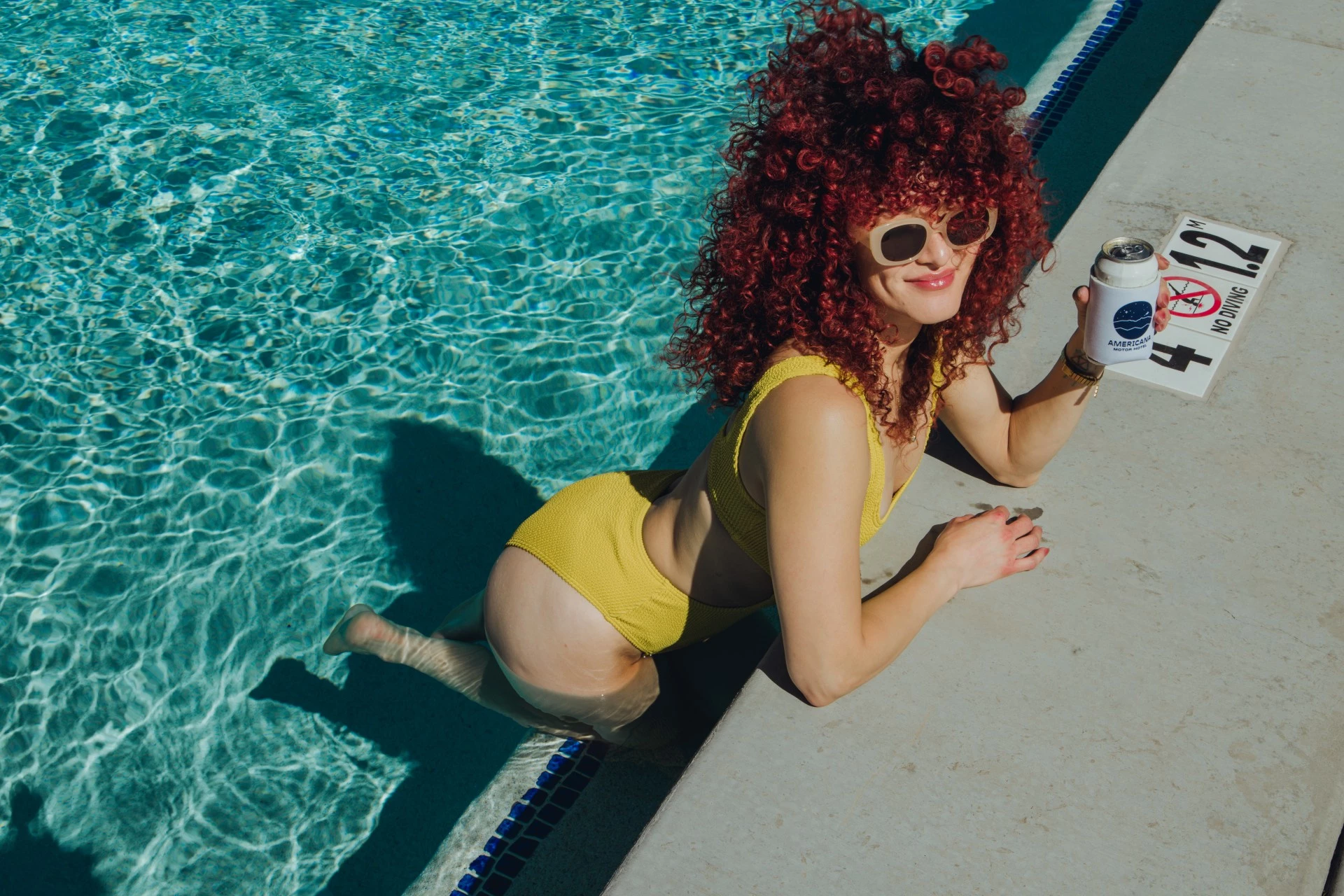 a woman in a yellow swimsuit and sunglasses holding a can