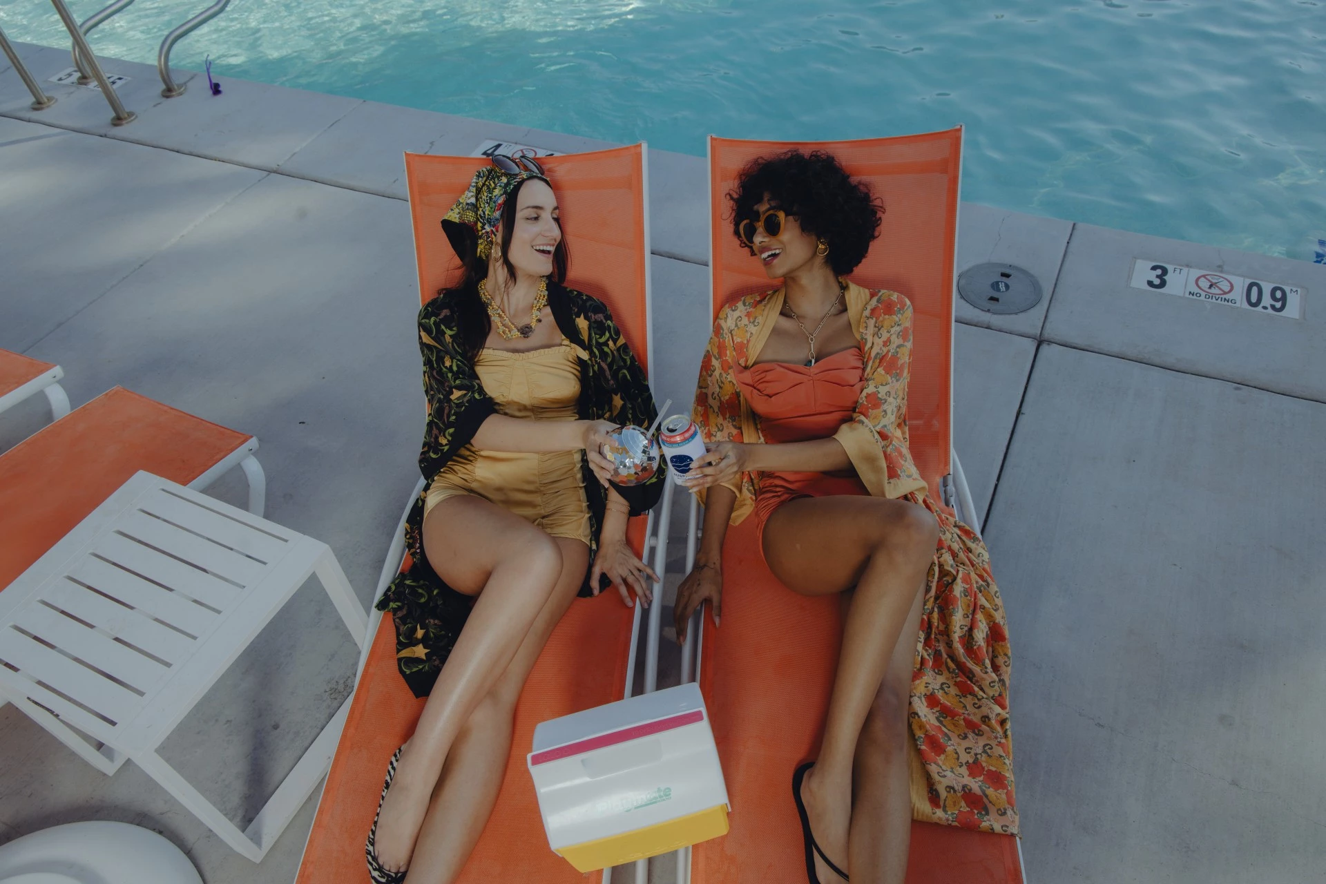 two women sitting on lounge chairs by a pool