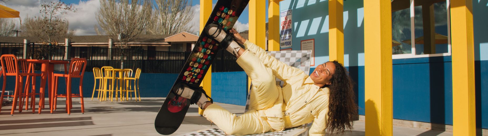 a person in a yellow suit lying on a bench with a snowboard