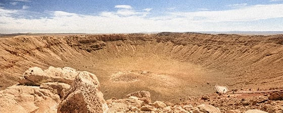 a rocky landscape with a few large rocks with Meteor Crater in the background