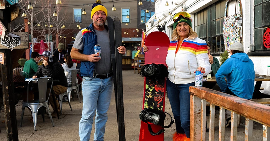 a man and woman holding snowboards and a drink