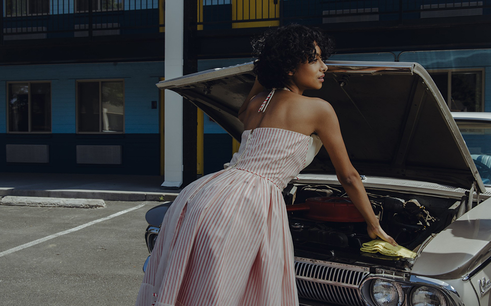 a woman in a dress looking at the hood of a car