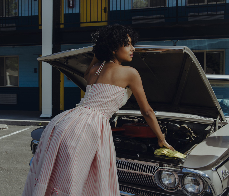 a woman in a dress standing by a car with the hood up