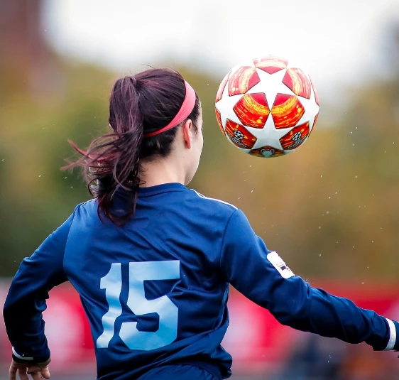 a woman in a blue jersey kicking a football ball