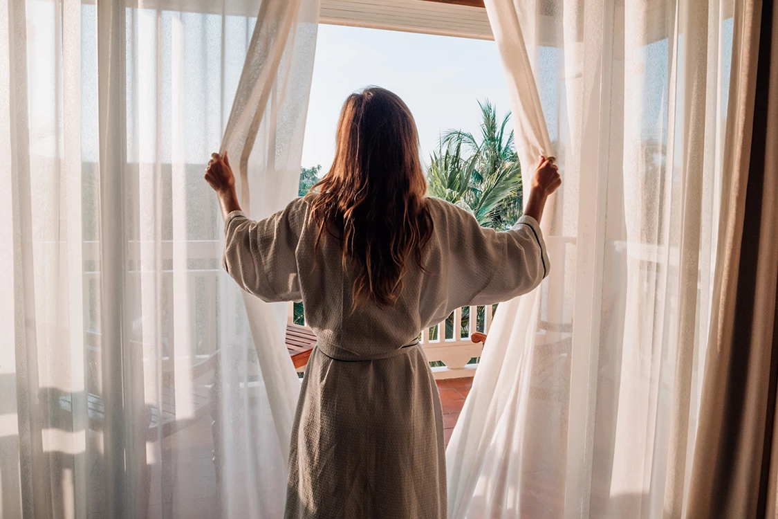 a woman opening curtains in a room