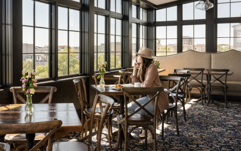 woman sitting on a table with flowers while having a croissant