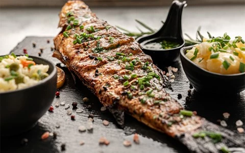 a piece of grilled fish with herbs on top, surrounded by bowls of food and a spoon