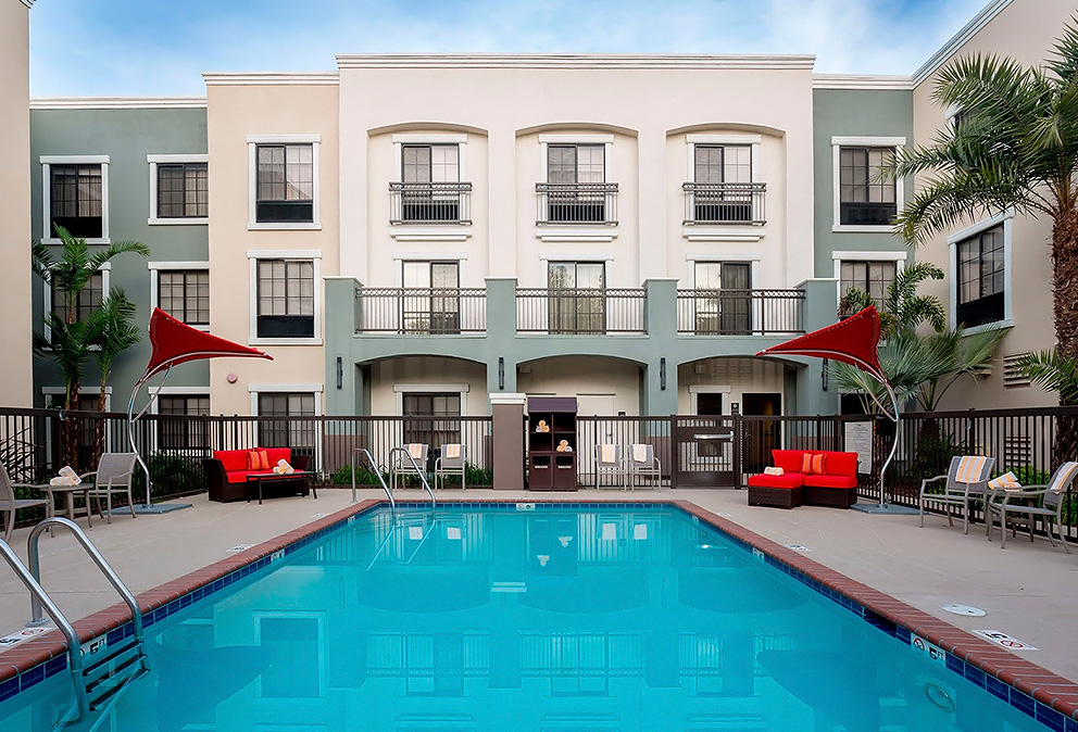 a swimming pool with red chairs and umbrellas in front of a building