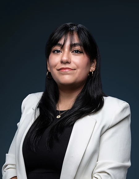 a woman with long black hair wearing a white blazer and gold earrings