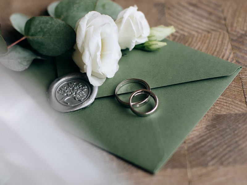 green envelope with tree wax stamp and wedding bands on the envelope with white flowers and green leaves also on it