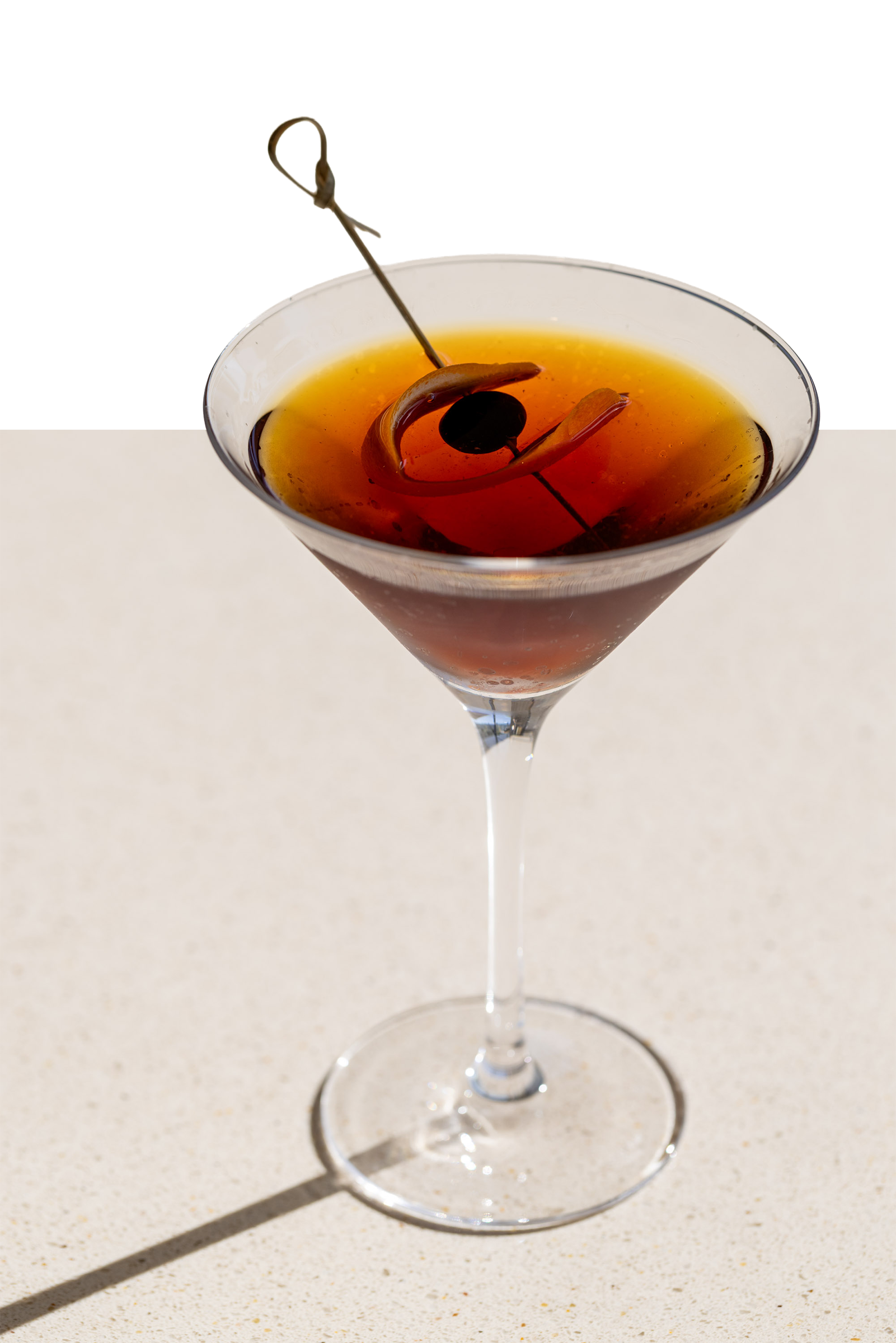 a glass with brown liquid and an olive on it