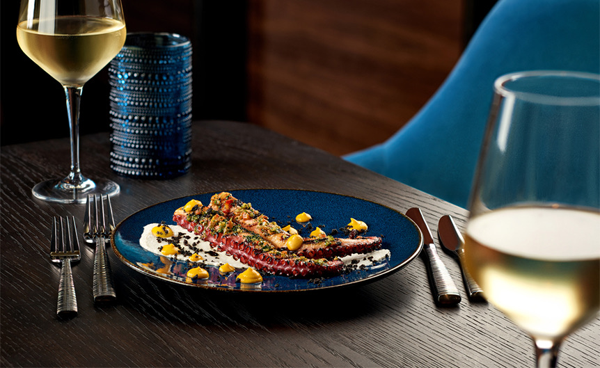 an octopus appetizer next to two glasses of white wine