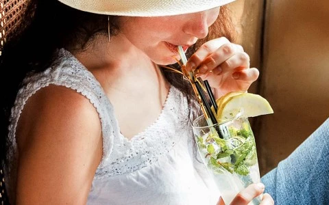 woman wearing a sun hat and a white shirt smelling a flower