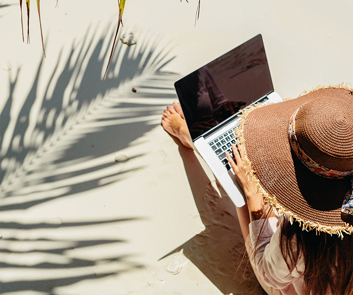 a woman sitting on the sand with a laptop