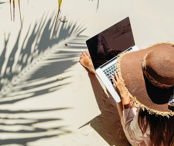 a woman sitting on the sand with a laptop