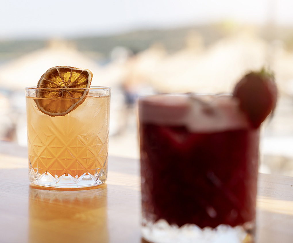 two glasses of liquid with a slice of orange on top of them