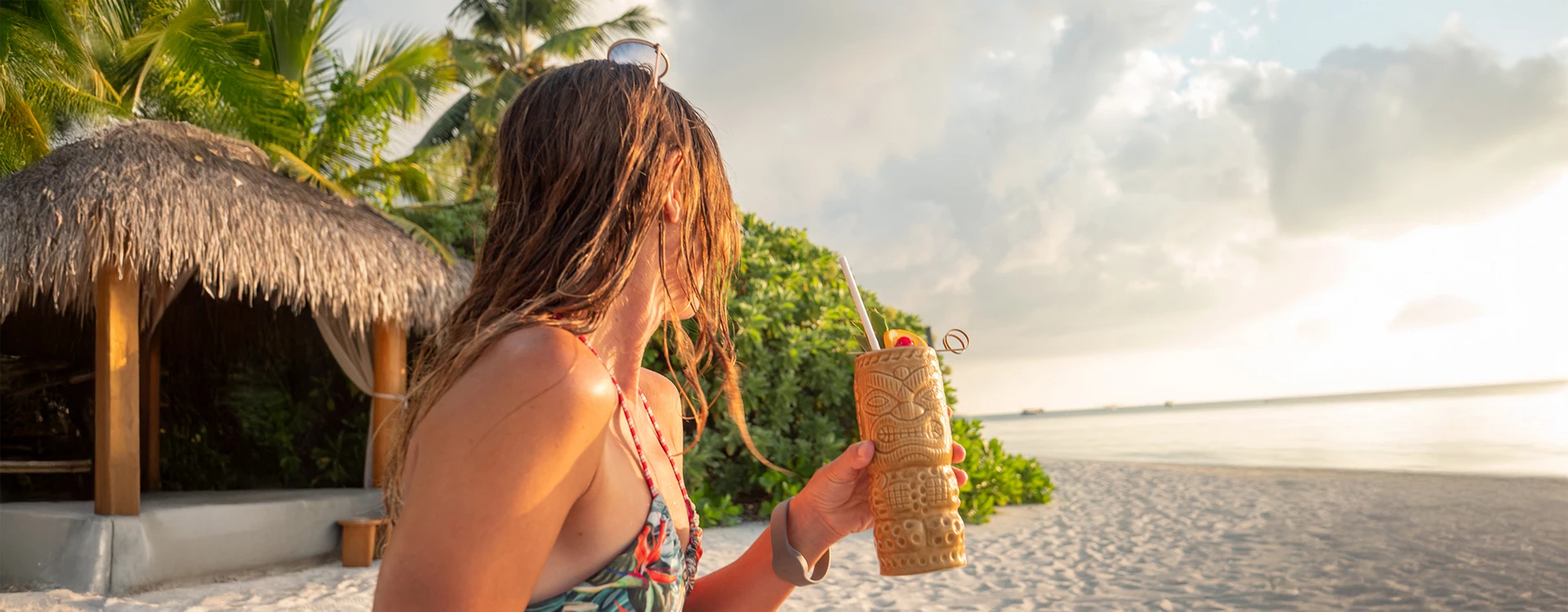 a woman holding a tiki glass on a beach